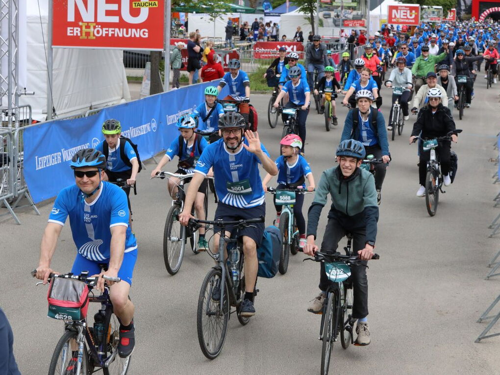 Eine große Gruppe Erwachsene und Kinder startet beim Fahrradfest. Manche lächeln und winken in die Kamera.