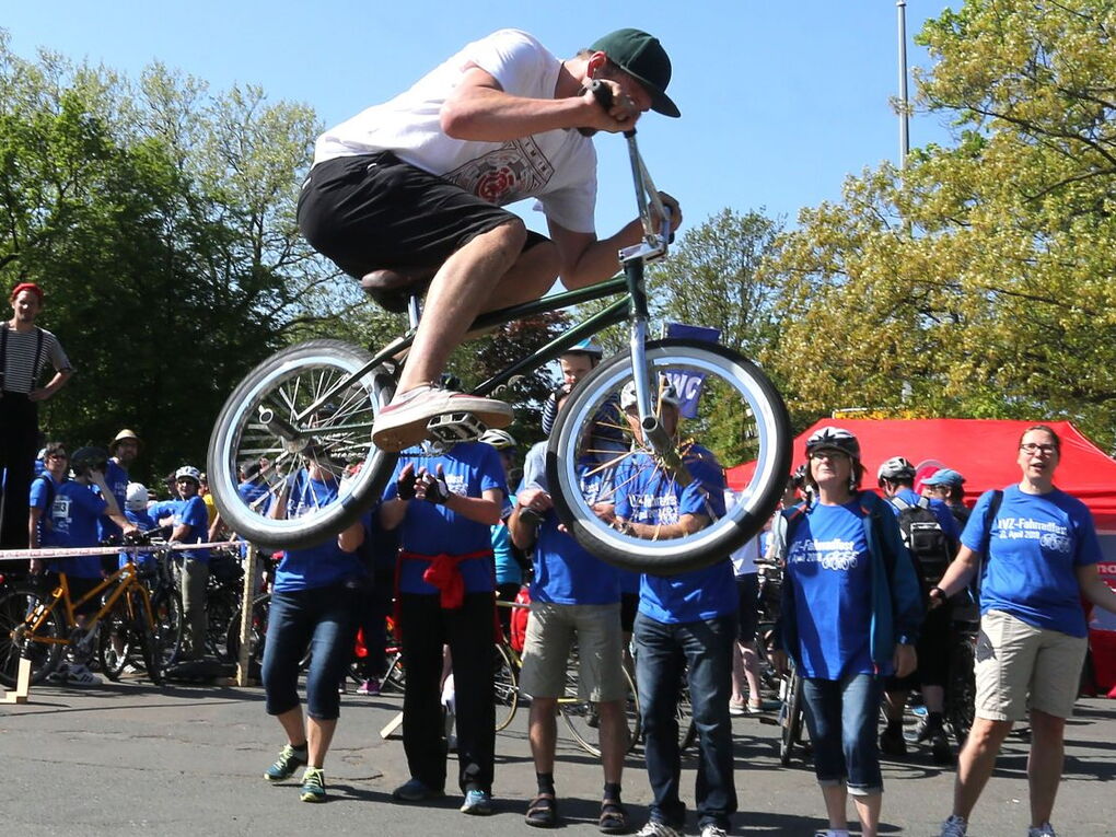 Ein BMX-Fahrer zeigt Kunststücke, mehrere Menschen in blauen Fahrradfest-T-Shirts schauen zu.