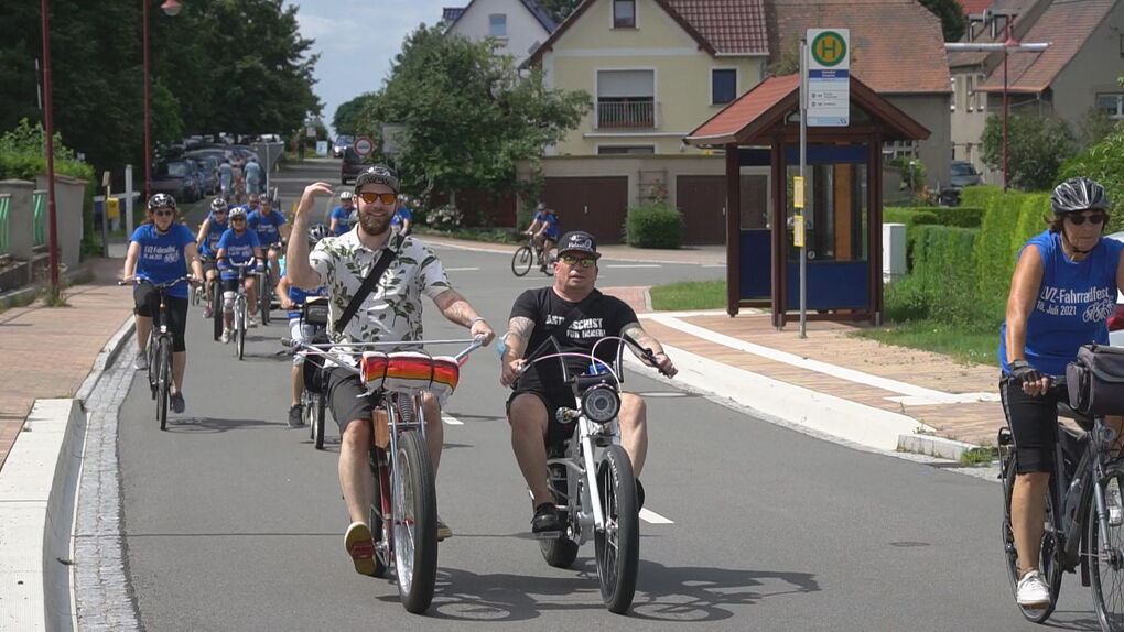 Mehrere Personen radeln entspannt durch ein Dorf.