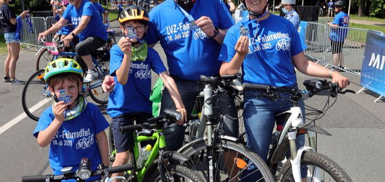 Eine Familie mit Mutter, Vater und zwei Kindern mit Fahrrädern halten stollz ihre Fahrradfest-Medaillen in die Kamera.