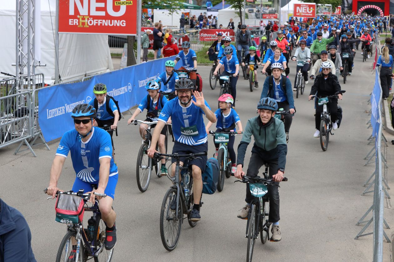 Eine große Gruppe Erwachsene und Kinder startet beim Fahrradfest. Manche lächeln und winken in die Kamera.